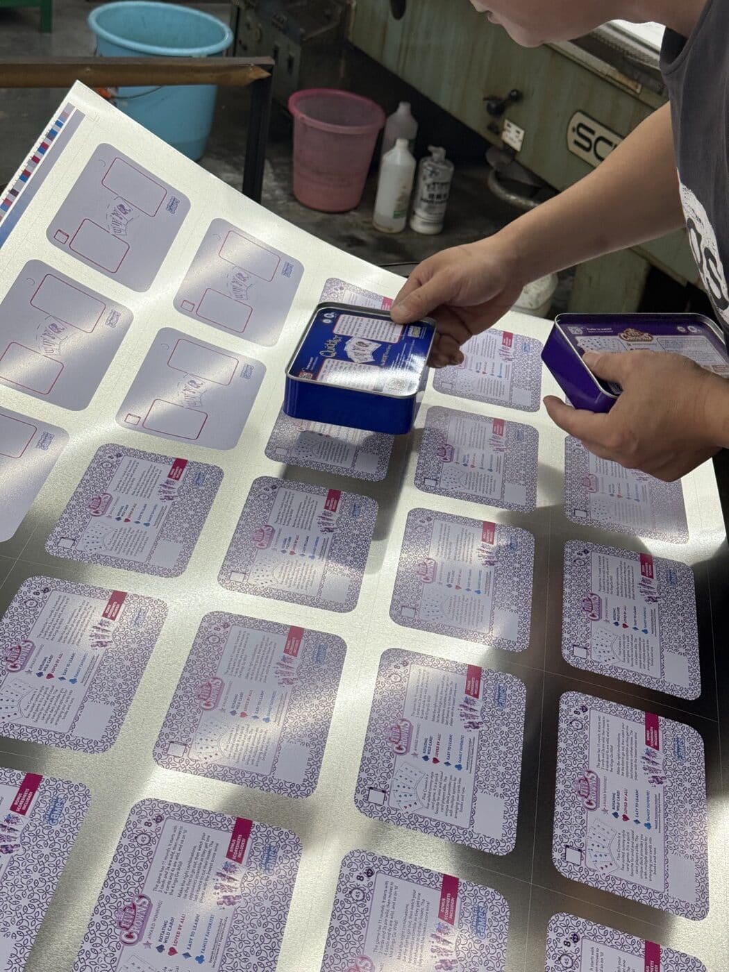 Junmei worker comparing finished tins with printed tinplate artwork